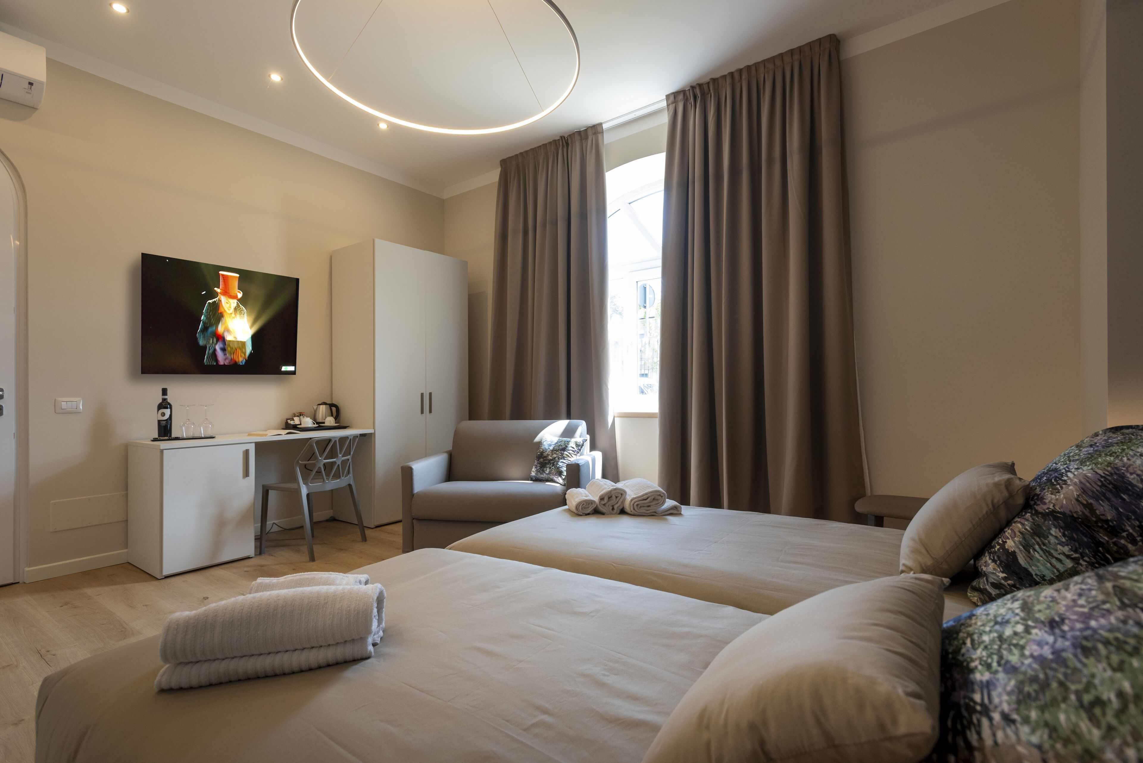 A modern hotel room with a large bed, a desk, a chair, and a television.