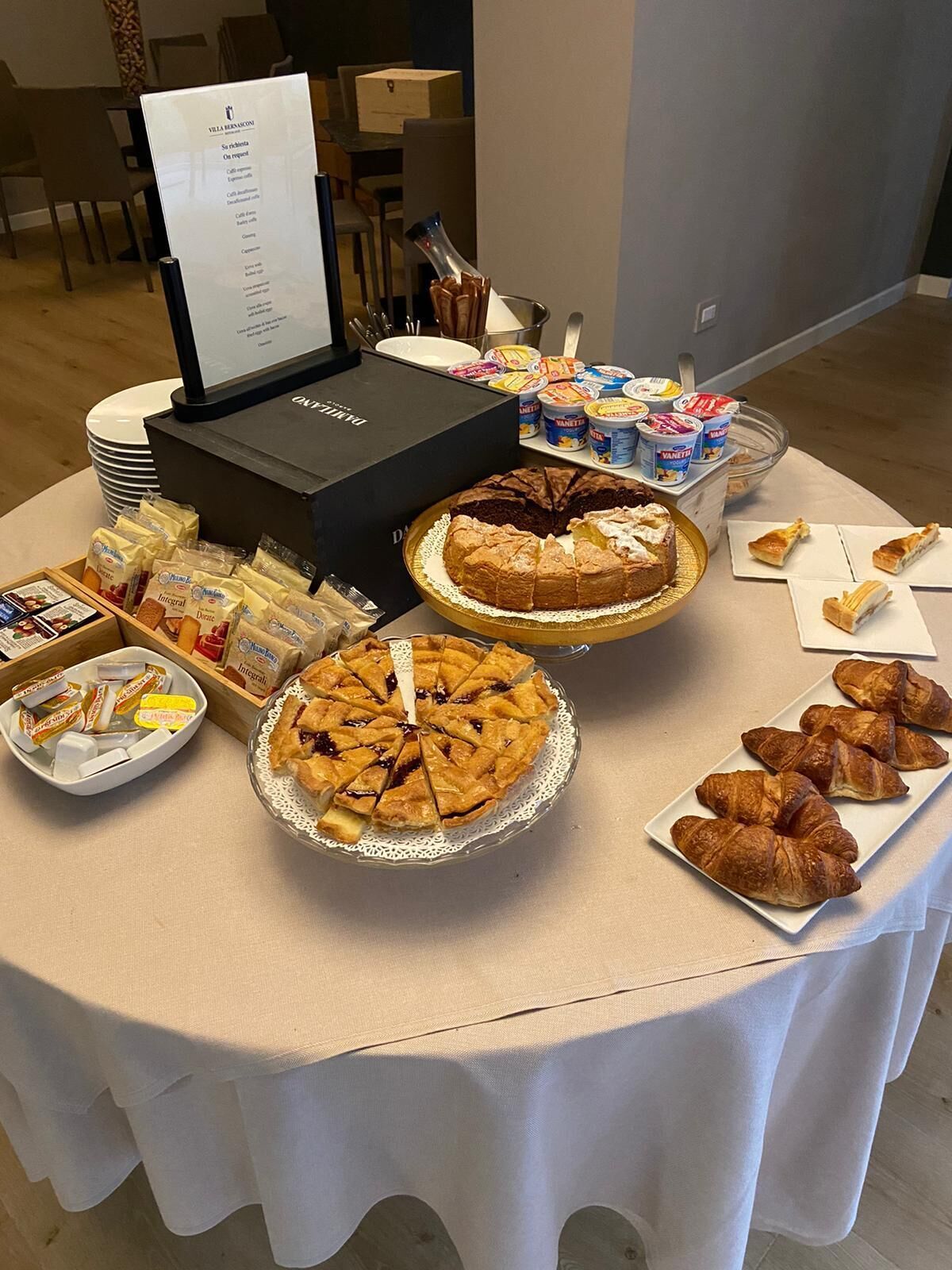 Una mesa de bufé con diversos alimentos, incluyendo pasteles, una tarta y recipientes de yogur.