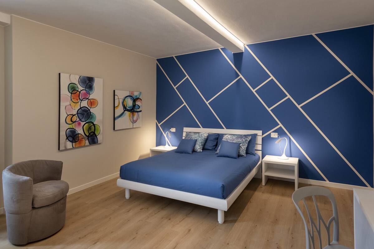 A bedroom with a bed, two nightstands, a chair, and artwork on the wall.