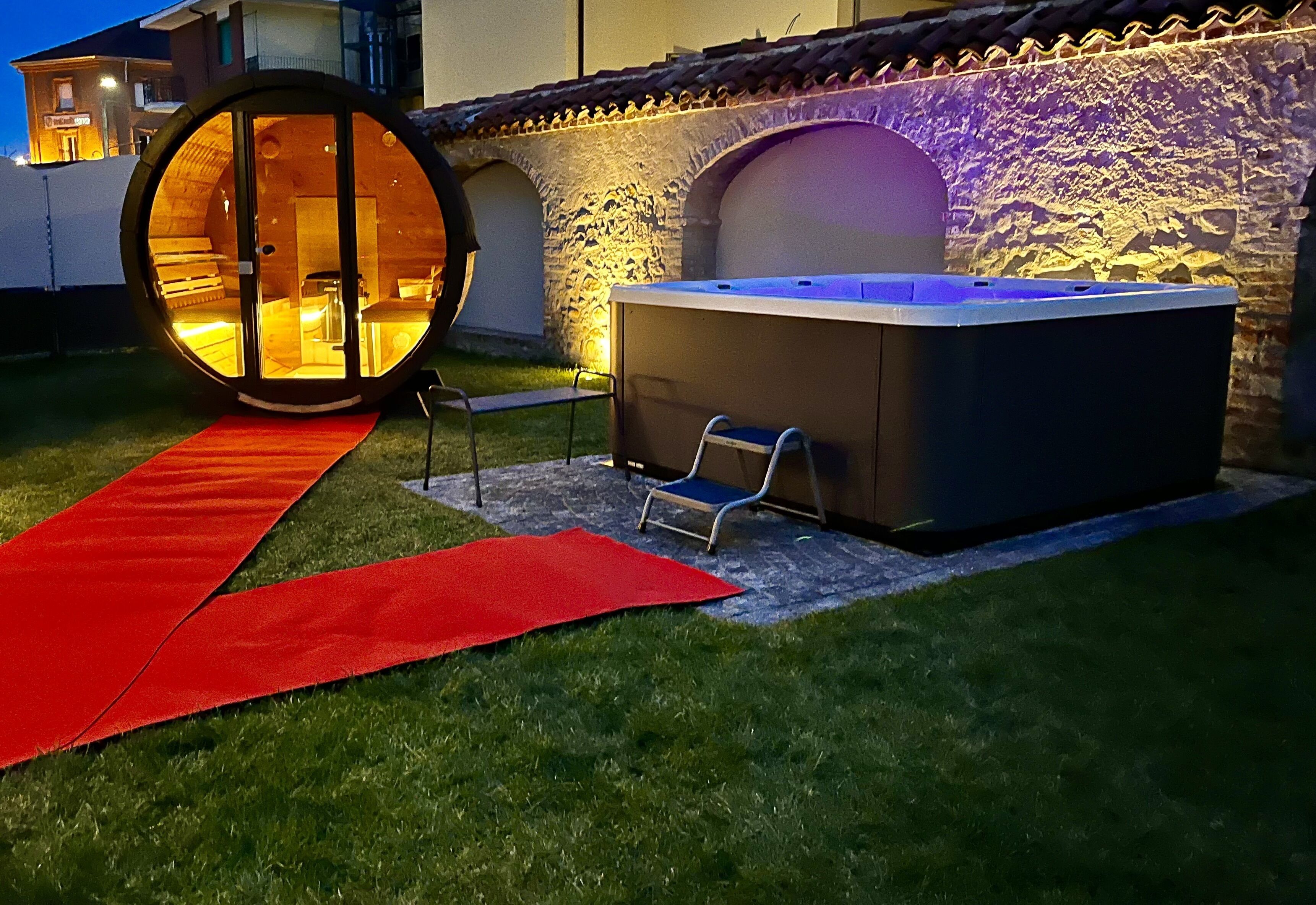 A circular hot tub with a red carpet leading to it, a stone wall, and a small chair.
