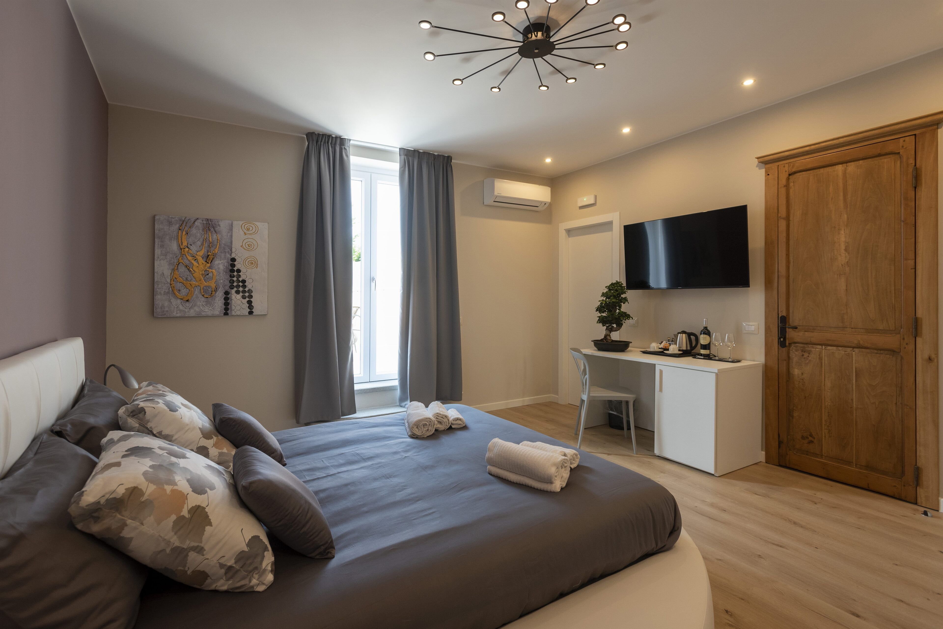 A modern bedroom with a large bed, a desk, a TV, and a wardrobe.