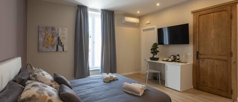 A modern bedroom with a large bed, a desk, a TV, and a wardrobe.