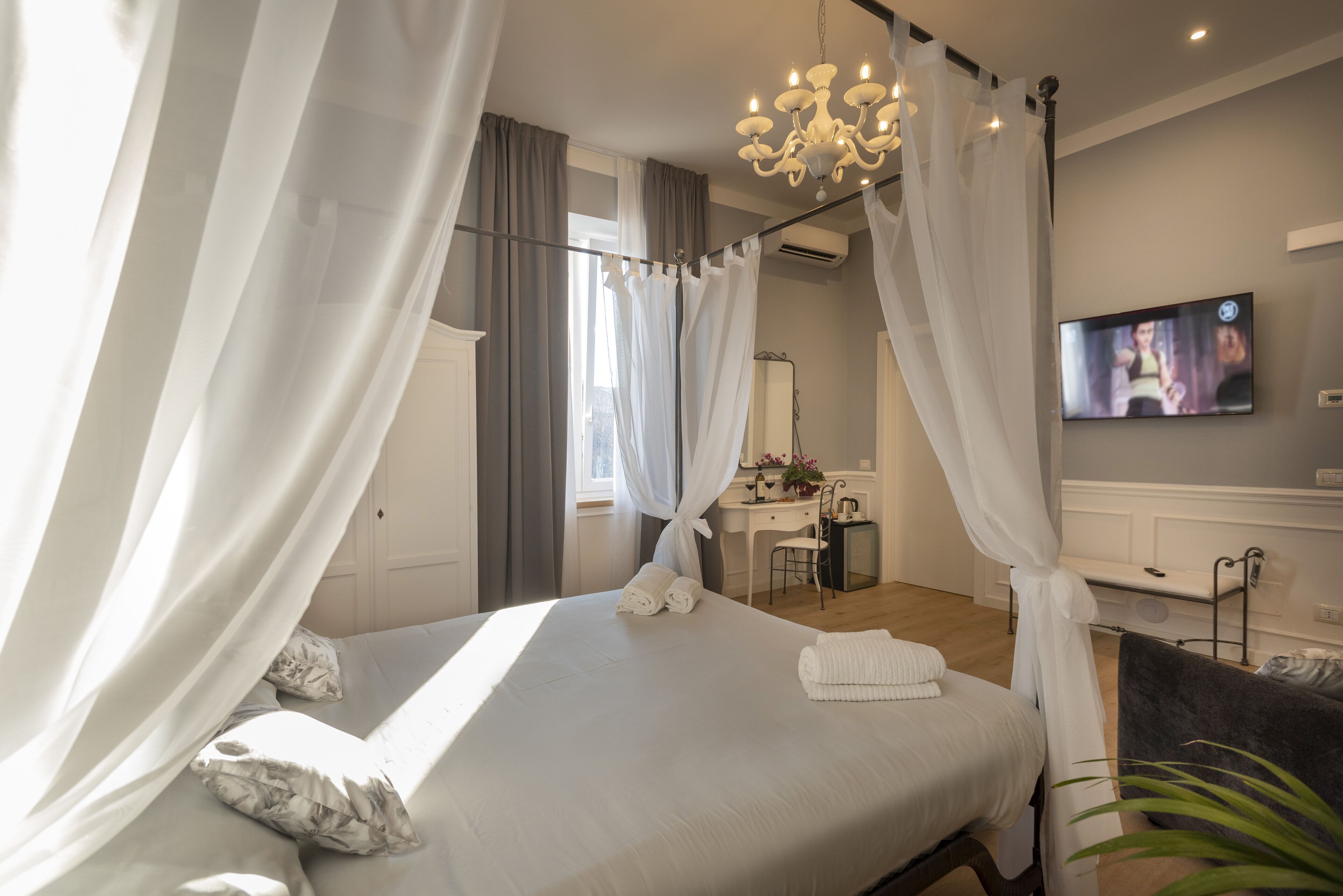 A bedroom with a bed, curtains, a desk, a chair, a TV, and a plant.