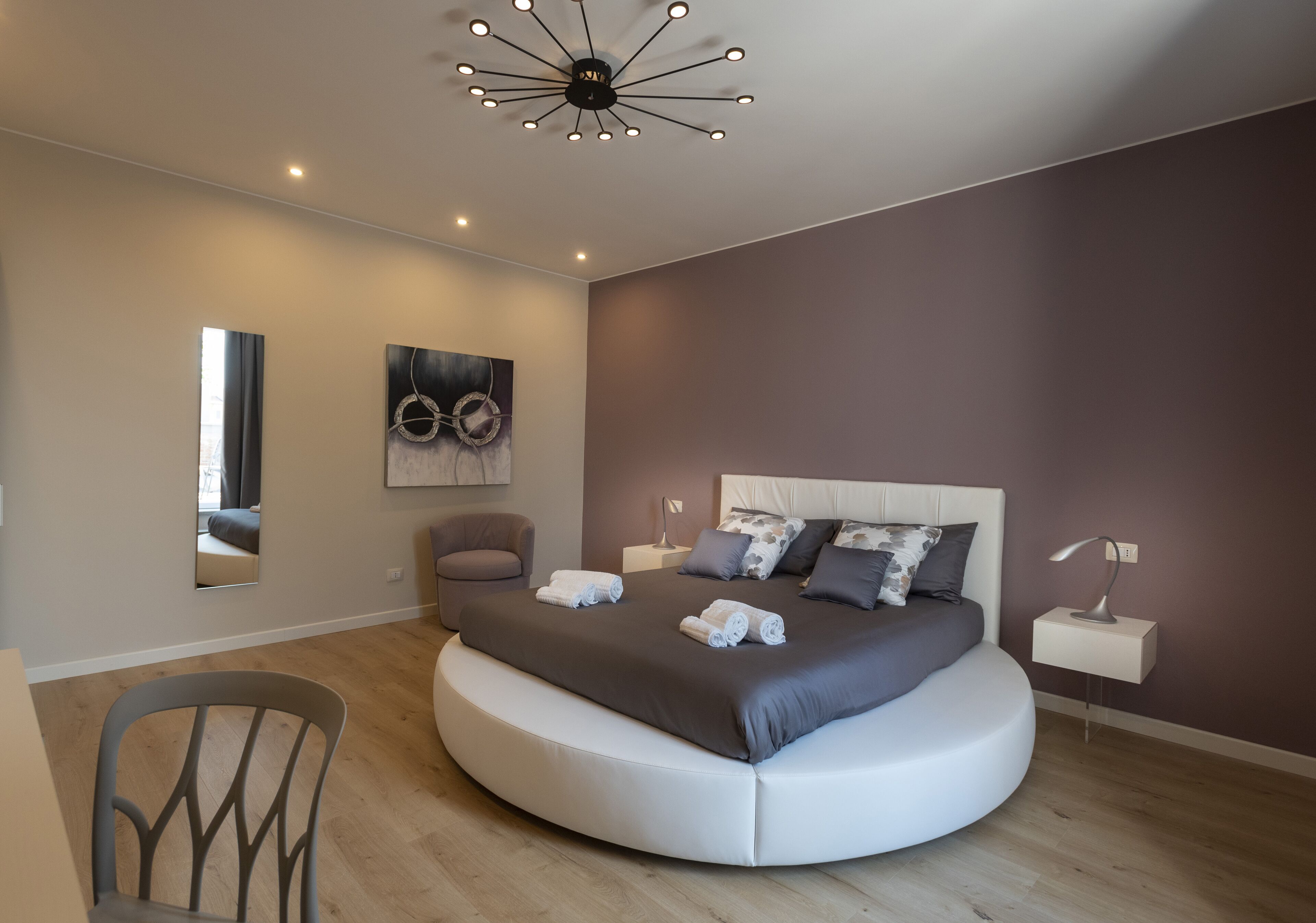 Ein modernes Schlafzimmer mit einem gebogenen Bett, einem runden Sessel, einem Nachttisch und einer Deckenleuchte.