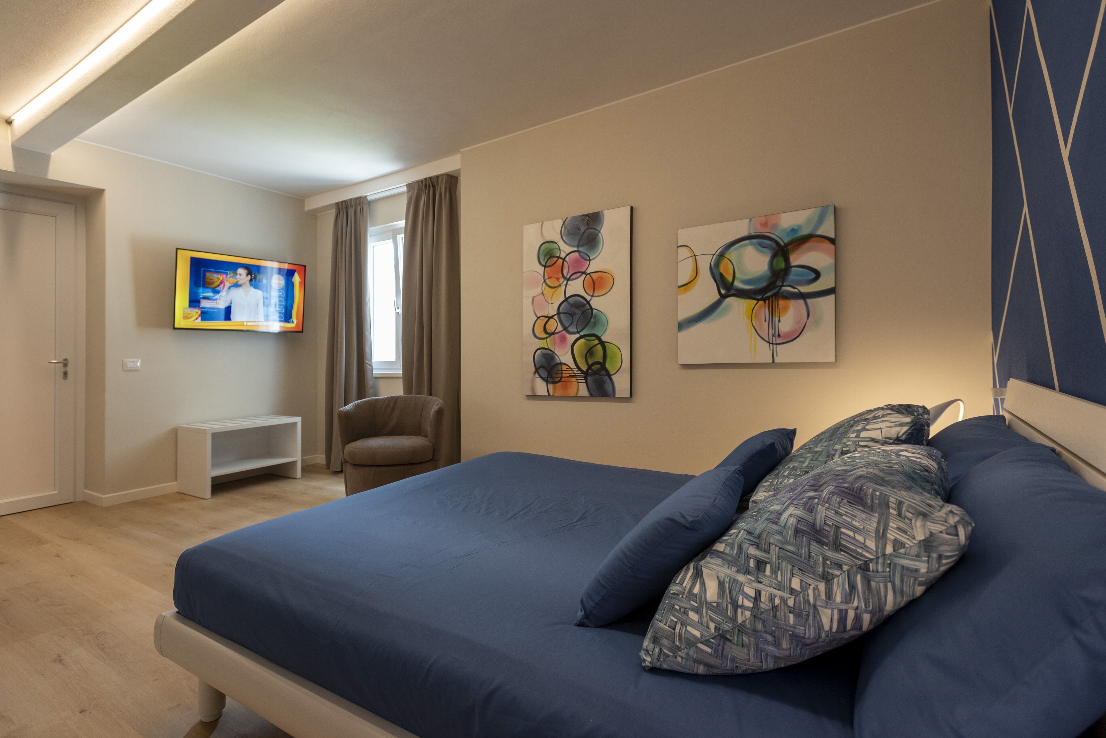 A bedroom with a large bed, a TV mounted on the wall, and abstract art pieces.