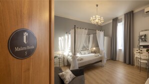 A bedroom with a four-poster bed, a sitting area with a sofa, a desk with a chair, and a mirror on the wall. - Villa Bernasconi - camere e ristorante - (Narzole)
