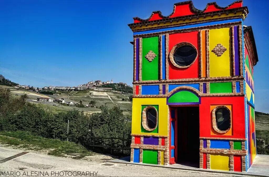 Une structure colorée, composée de plusieurs pièces, dotée d’une porte et de fenêtres, qui se détache sur un paysage rural.