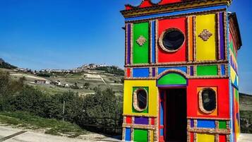 Une structure colorée, composée de plusieurs pièces, dotée d’une porte et de fenêtres, qui se détache sur un paysage rural.