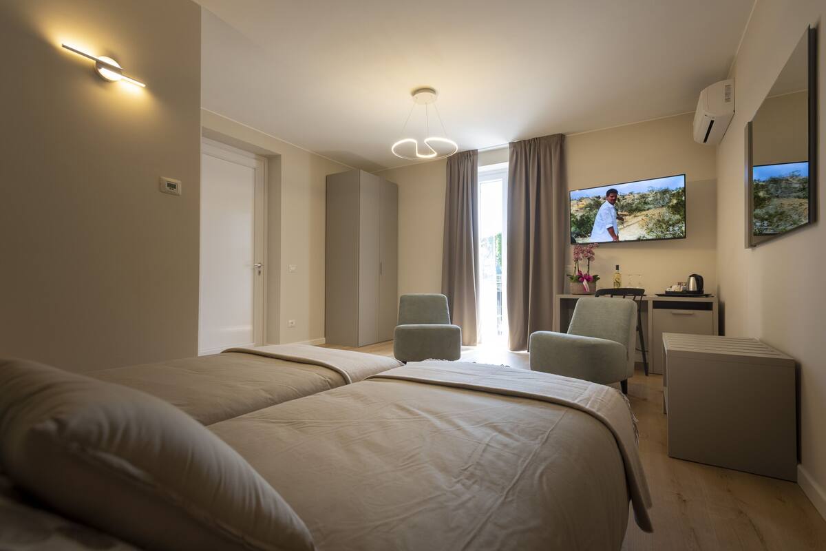 A hotel room with two beds, a desk, a chair, a TV, and a window with curtains.