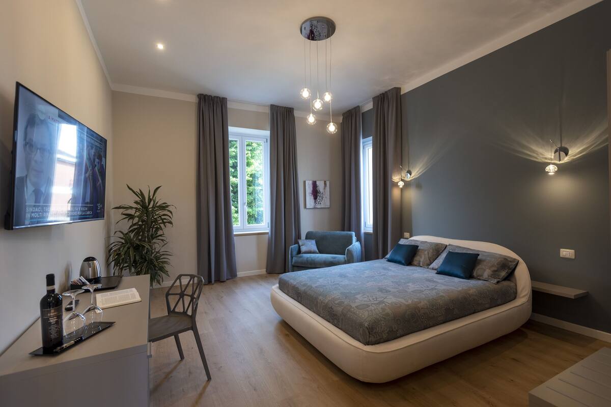 A modern bedroom with a large bed, a desk with a computer, and a TV on the wall.