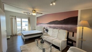 A modern bedroom with a bed, a sofa, a glass coffee table, and a large painting of a landscape. - Ferienhaus Breisach by Interhome (Breisach)
