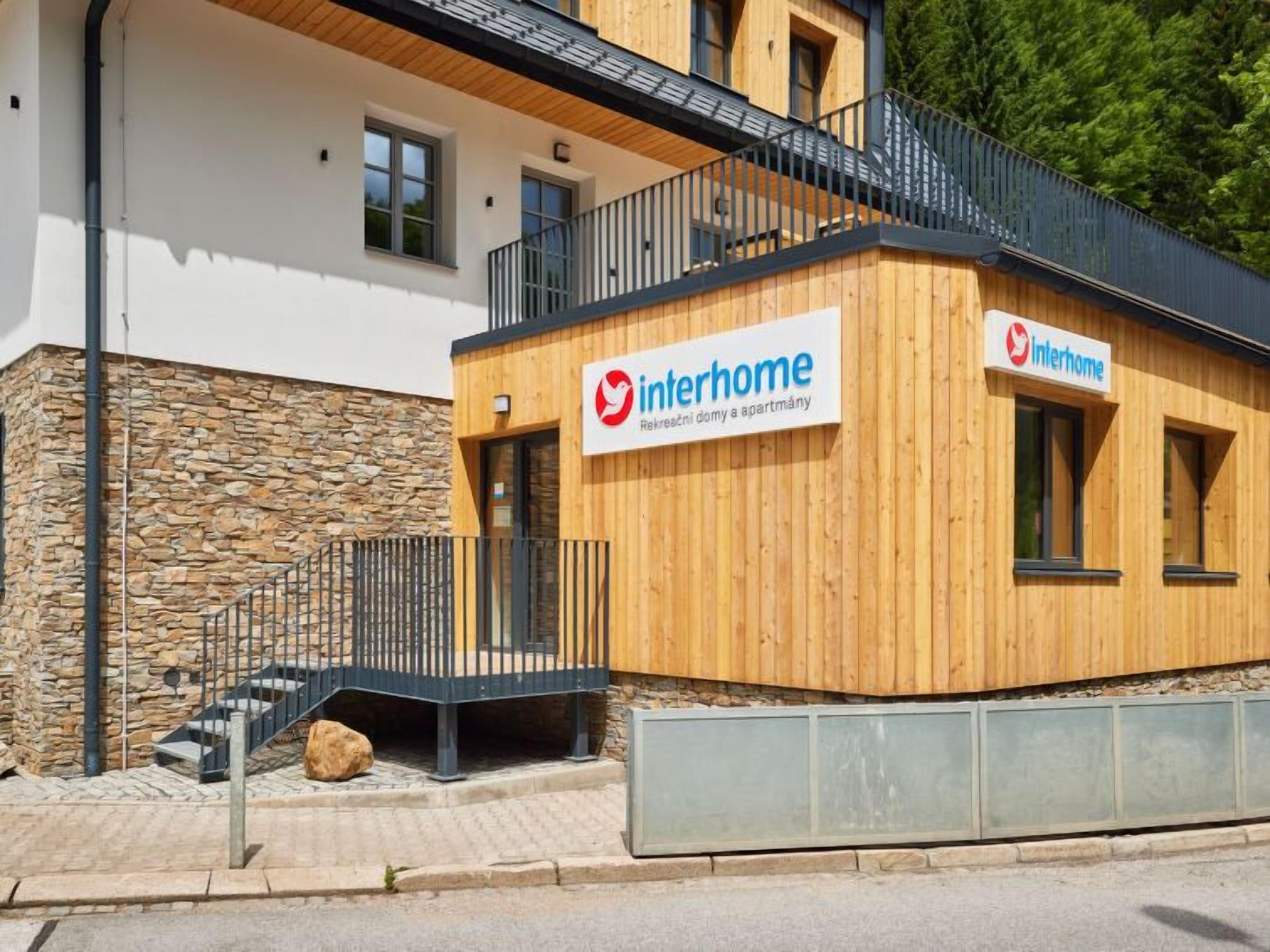 A modern building with a wooden facade and a stone base. It has a sign reading "Interhome" indicating it is a residential property.