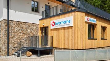 A modern building with a wooden facade and a stone base. It has a sign reading "Interhome" indicating it is a residential property.