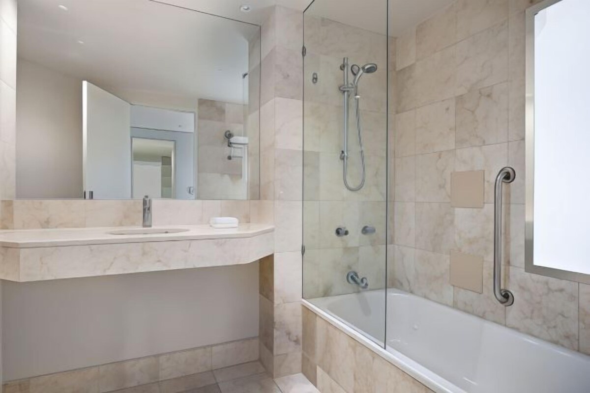 A modern bathroom with a glass-enclosed shower, a white bathtub, and a marble vanity.