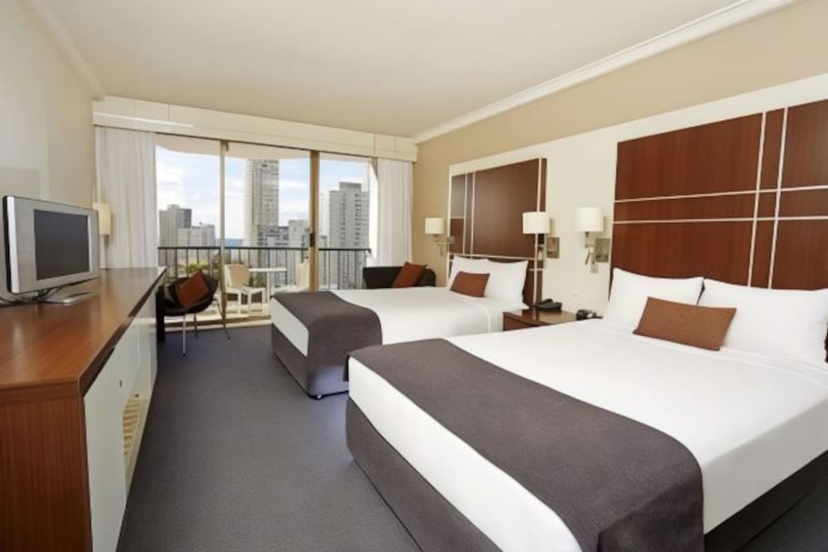 Une chambre d’hôtel avec deux lits, un bureau avec une télévision et un balcon offrant une vue sur la ville.