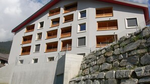 Un edificio de varios pisos con techo rojo y numerosas ventanas, rodeado por un muro de piedra.