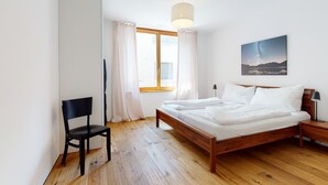 Un dormitorio con una cama de madera, una silla, una mesita de noche, una lámpara y una ventana con cortinas.