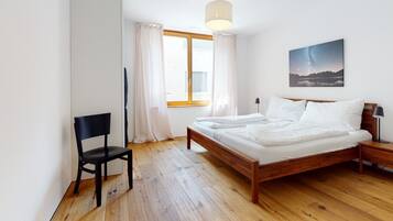 Une chambre à coucher avec un lit en bois, une chaise, une table de chevet, une lampe et une fenêtre avec des rideaux.