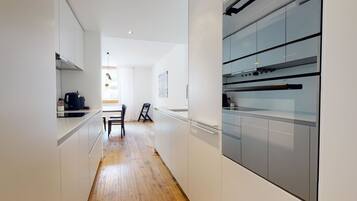 Une cuisine moderne avec des meubles blancs, un plancher en bois et un coin repas comprenant une chaise et une table.