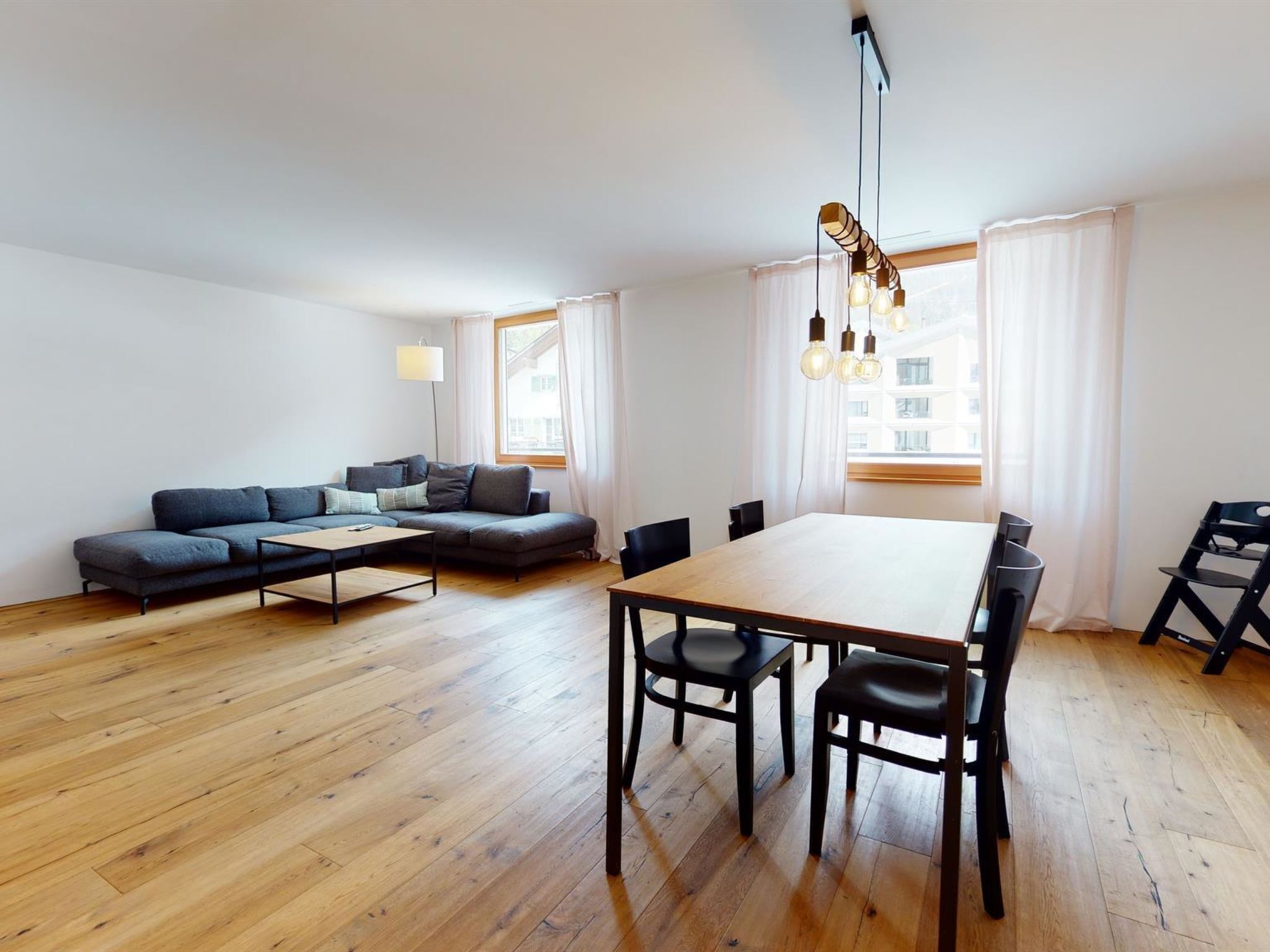 Un salon moderne avec un canapé, une table à manger et des chaises, ainsi qu’une lampe.