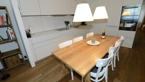 Eine moderne Küche mit weißen Schränken, einem Holztisch, weißen Stühlen und einem Einbauofen.