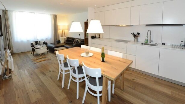 Eine moderne Küche mit weißen Schränken, einem Holztisch und vier weißen Stühlen.