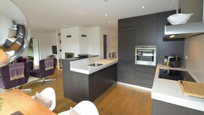 A modern kitchen with a central island, built-in oven, and a dining area with a wooden table and chairs. - Uehlinger Züger by Interhome (Valbella)
