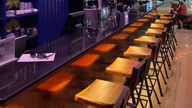 A bar area with a long counter, wooden stools, and shelves with various items. - Neptuna Kata Hotel (Karon)
