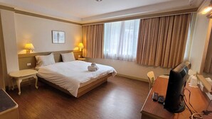 A hotel room with a bed, bedside tables, a desk with a computer, and a window with curtains. - Neptuna Kata Hotel (Karon)