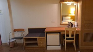 A small, compact bedroom with a single bed, a desk with a chair, a small refrigerator, and a wardrobe. - Neptuna Kata Hotel (Karon)