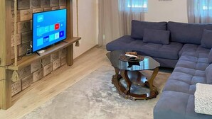 Un salón con pared de madera, un televisor de pantalla plana, un sofá de color oscuro y una mesa de centro de vidrio.