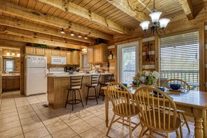 A wooden cabin-style kitchen with a central island, bar stools, and a dining table with chairs.