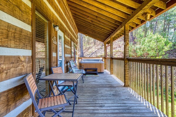 A wooden deck with a hot tub, seating, and a view of a forest.