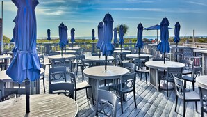 A deck with round tables and chairs, covered by blue umbrellas, overlooking a scenic view. - Ocean Front Condo with Resort Amenities, Short Walk to Beach (Hilton Head Island)