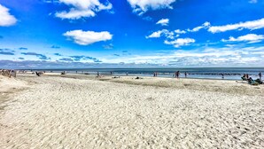 A wide sandy beach with people walking and relaxing, and a clear blue sky with clouds. - Ocean Front Condo with Resort Amenities, Short Walk to Beach (Hilton Head Island)