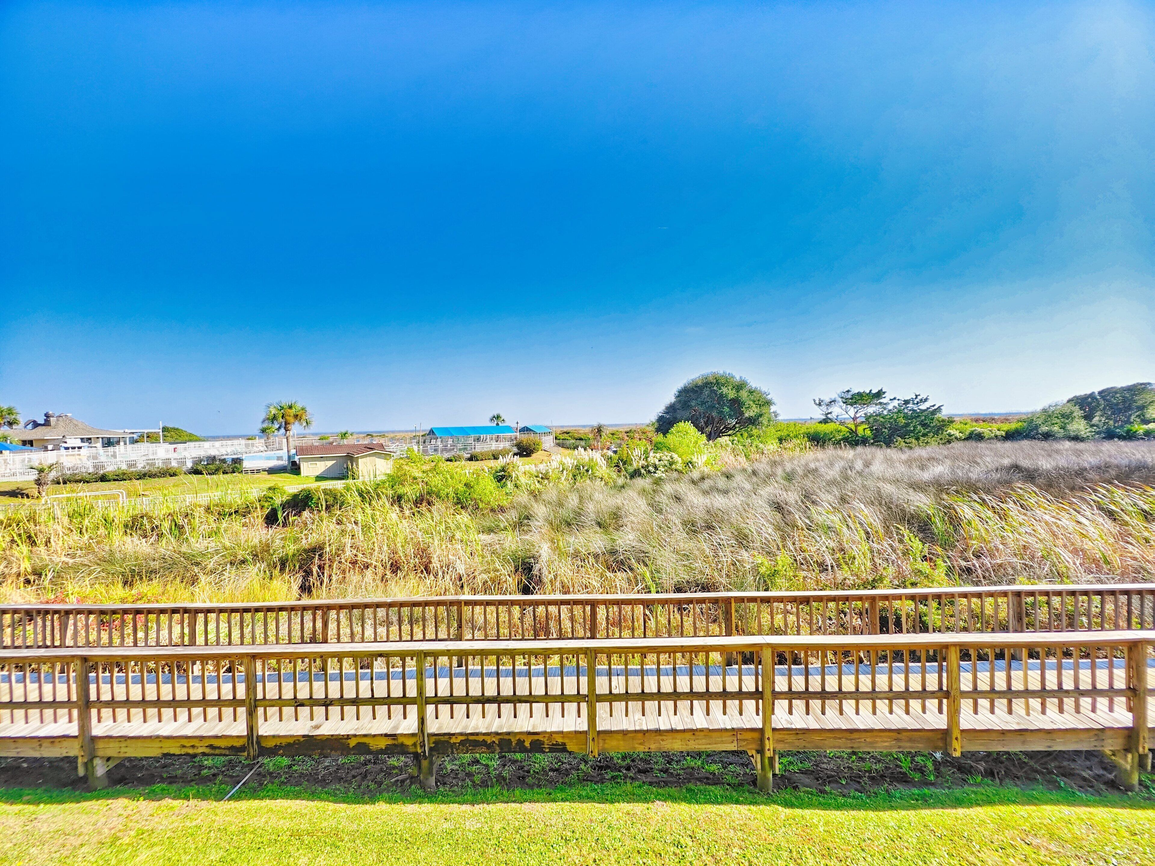 A wooden deck with a view of a grassy field and distant buildings.