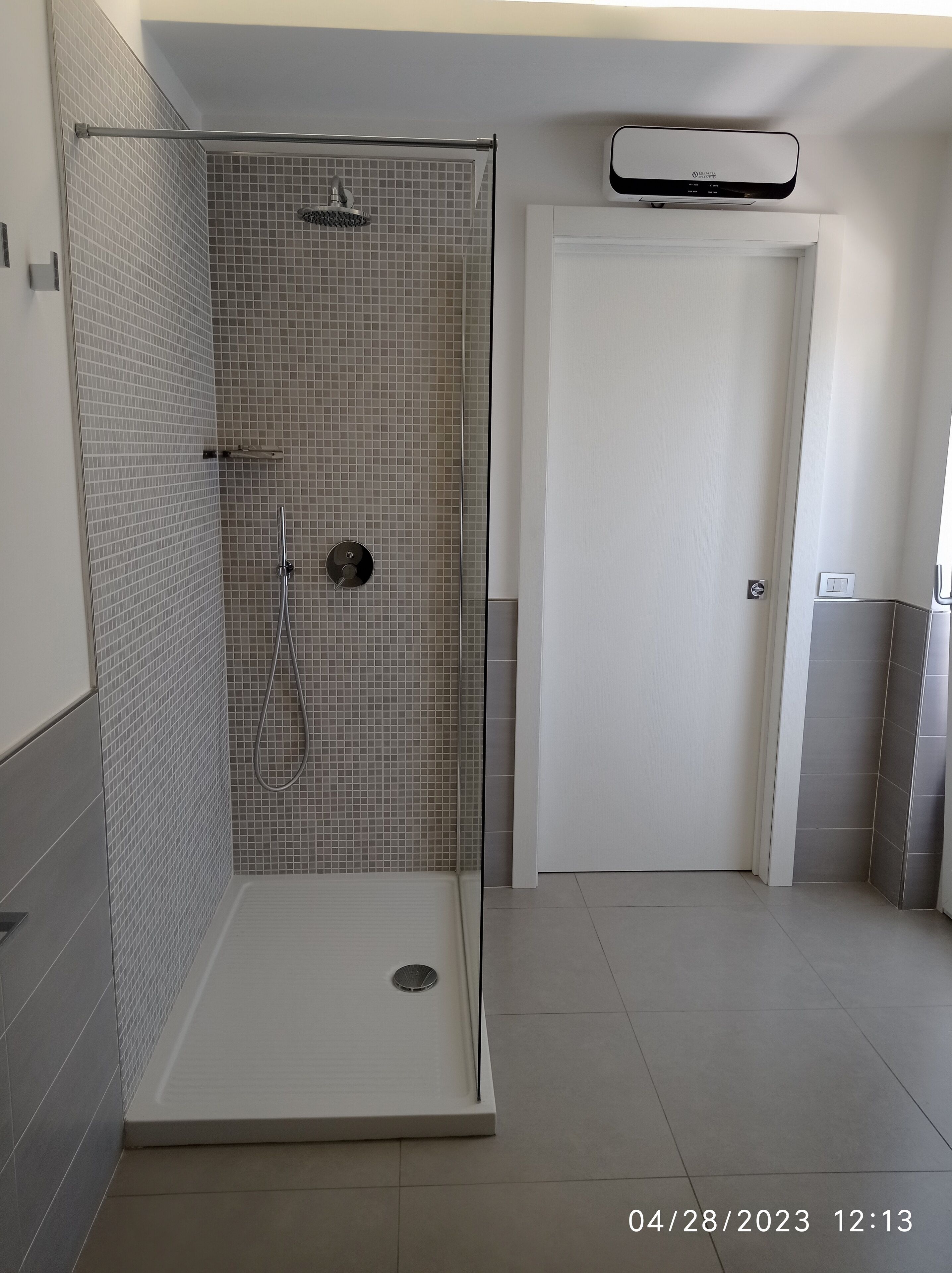 Une salle de bain moderne avec une douche à l’italienne, des murs carrelés et une porte blanche.
