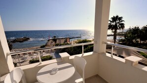 Un balcon avec une table et des chaises, donnant sur une plage bordée d’un palmier et offrant une vue sur l’océan.