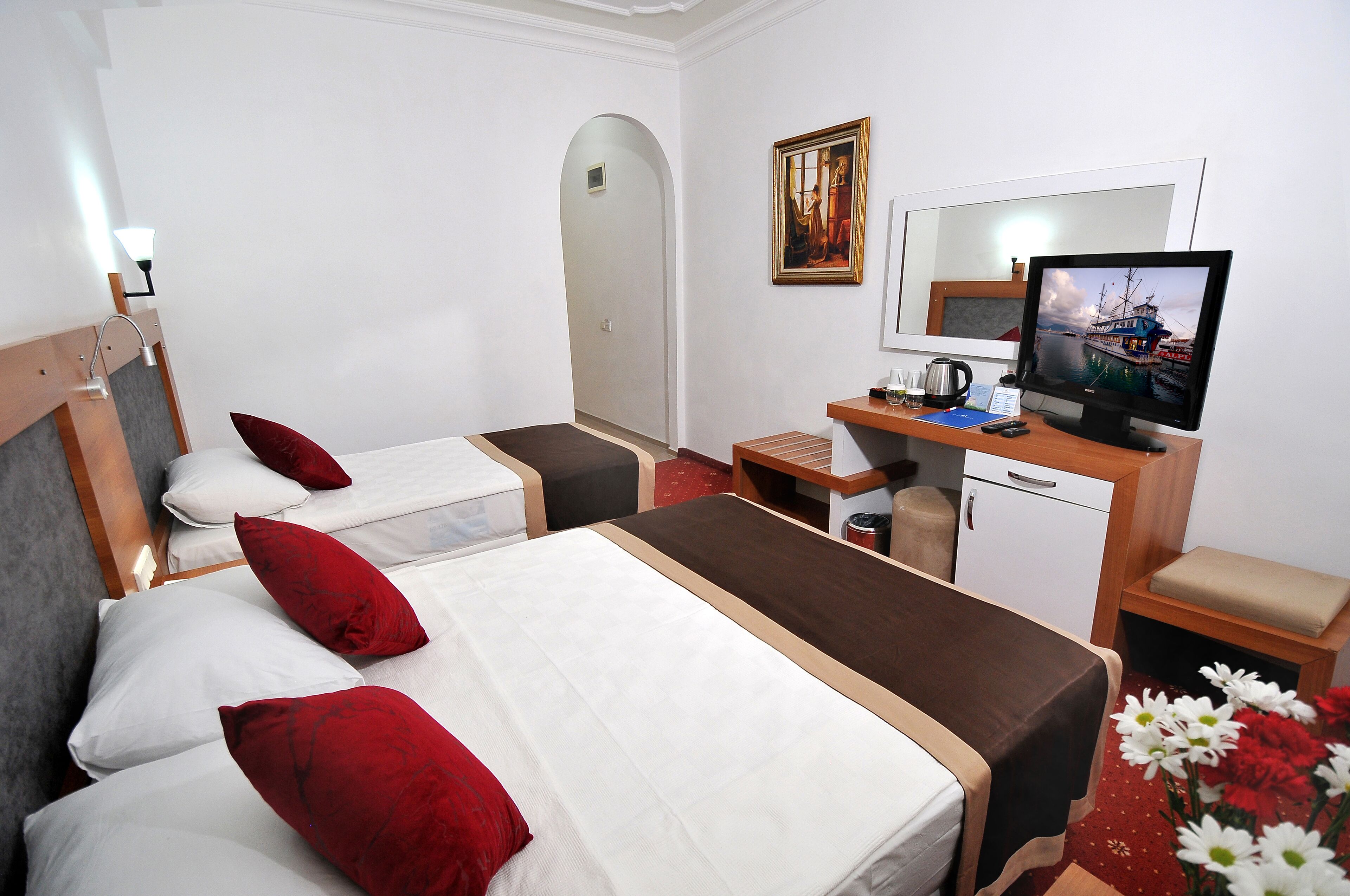 A hotel room with two beds, a desk with a computer, a mirror, and a painting on the wall.