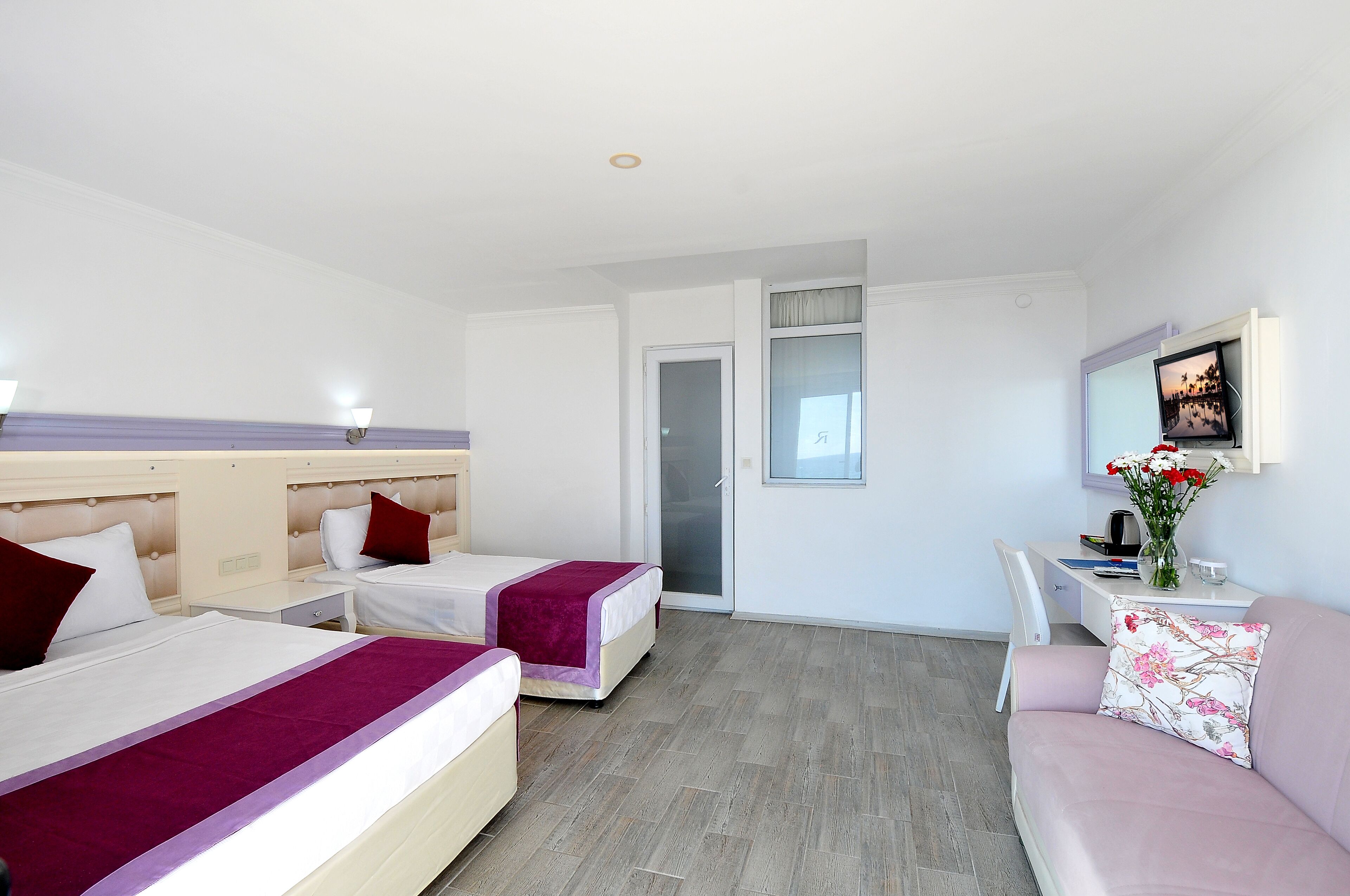A hotel room with two beds, a sofa, a desk, and a TV.