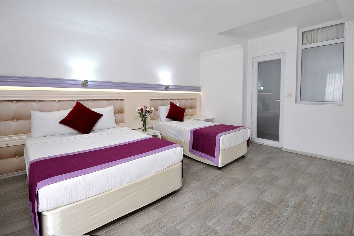 A hotel room with two beds, a nightstand with a vase of flowers, and a large window with a view.