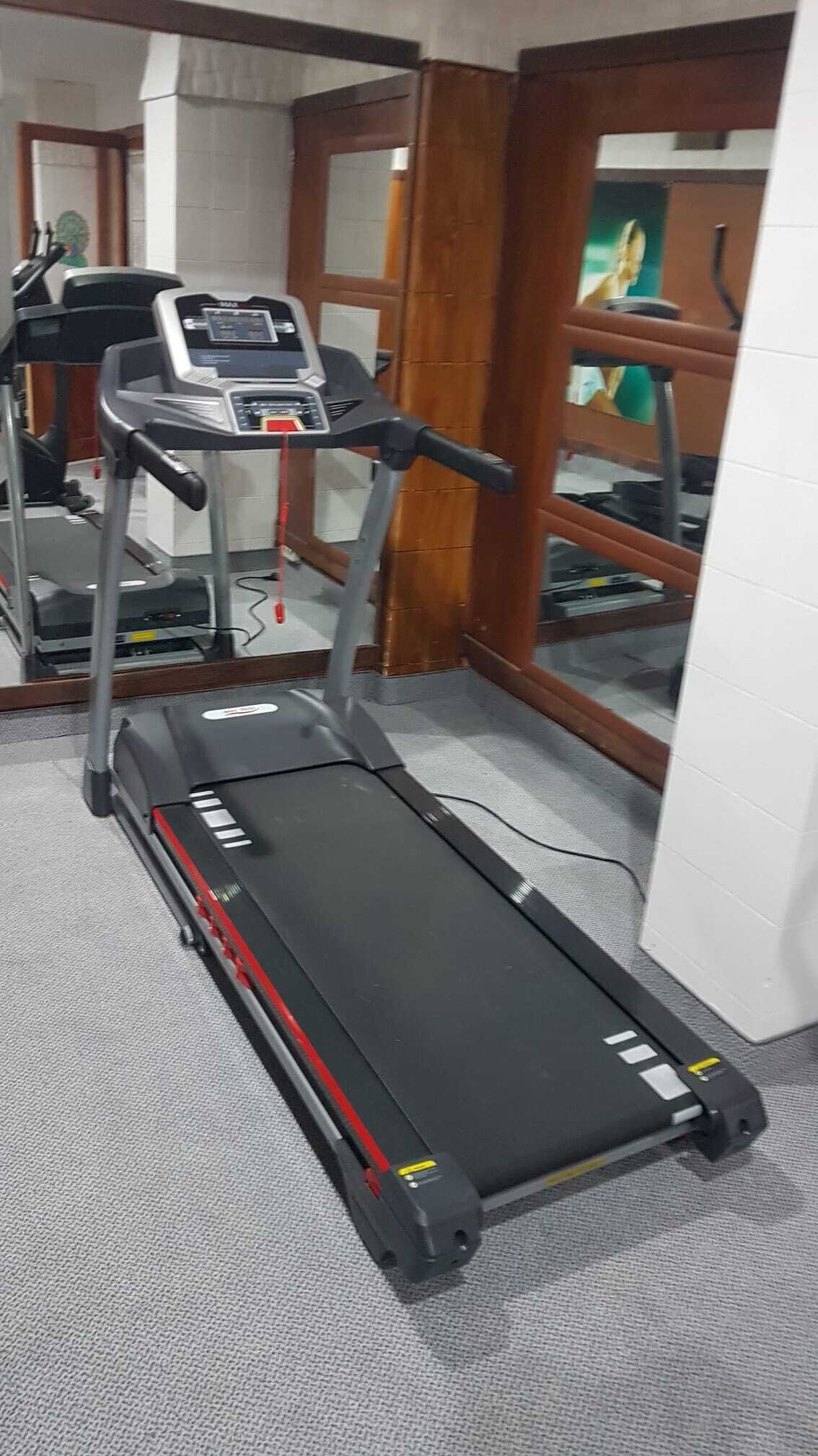 A treadmill in a room with a carpeted floor and a wooden door.