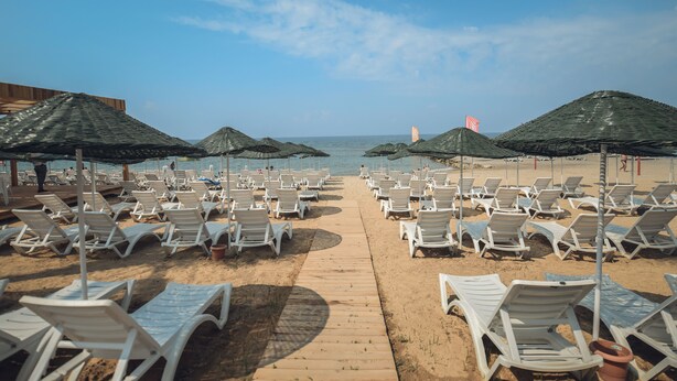 Une plage bordée de rangées de chaises longues blanches et de parasols, une promenade en bois et l’océan en toile de fond.
