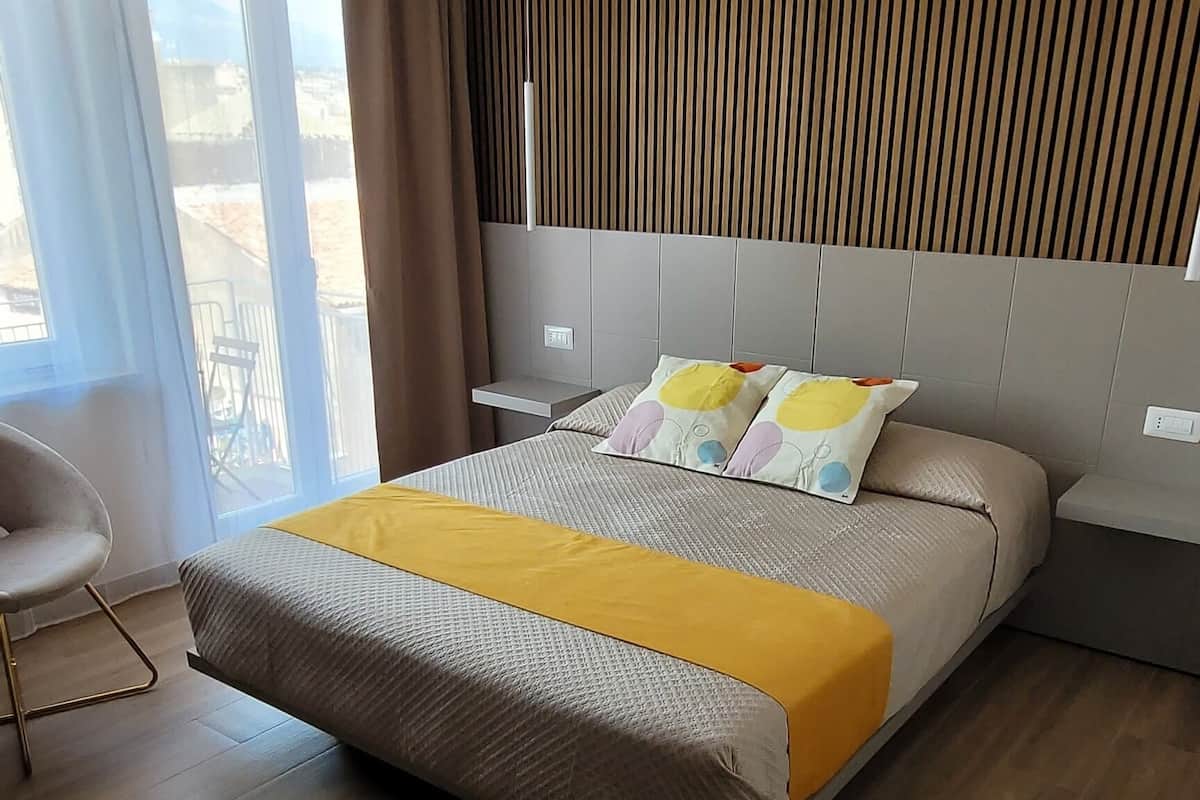 A modern bedroom with a large bed, a chair, and a view of the outdoors.
