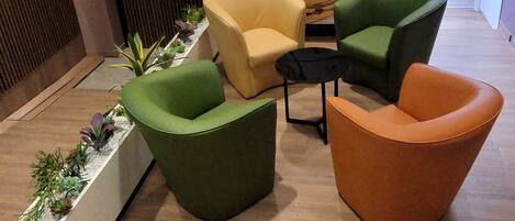 Un espace détente moderne avec des fauteuils verts et orange, un fauteuil jaune et un pot de fleurs blanc contenant des plantes.