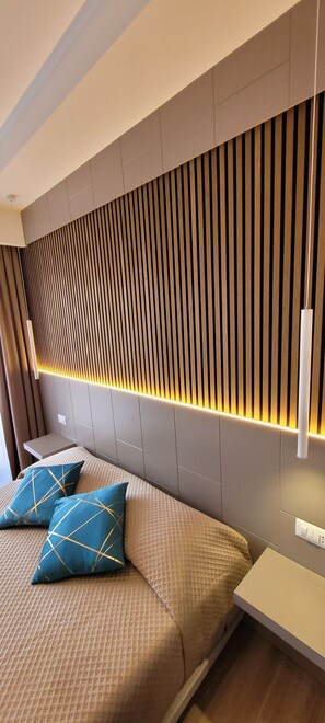 A modern bedroom with a bed, two pillows, a bedside table, and a wall with vertical slats and under-cabinet lighting. - TH LUXURY CENTRAL (Catania)