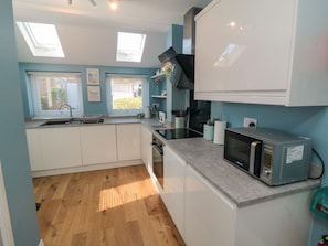 A modern kitchen with skylights, white cabinets, a microwave, and wooden flooring.