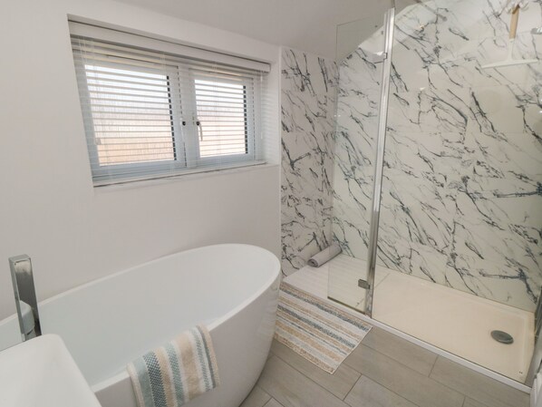 A bathroom with a freestanding bathtub, a shower with a glass door, and a window with blinds.