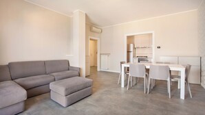 Una sala de estar moderna con un sofá modular, una mesa de comedor con sillas y una cocina con armarios y electrodomésticos.