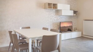 Una sala de estar moderna con una mesa de comedor blanca, seis sillas, un televisor de pantalla plana y estanterías empotradas sobre el televisor.